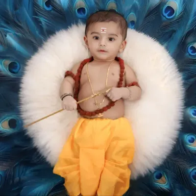 A beautiful portrait of a baby boy dressed as Lord Muruga, looking directly at the camera with a sweet expression. The backdrop of peacock feathers adds a touch of divine splendor.