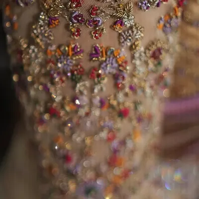 A macro shot of a bridal blouse sleeve, showing the texture and dimension of hand set Zardozi and colorful threadwork. This level of detail is what makes a custom piece truly special.