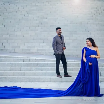 A grand, elegant portrait for the expecting couple. The flowing gown and architectural background create a sense of timeless sophistication.