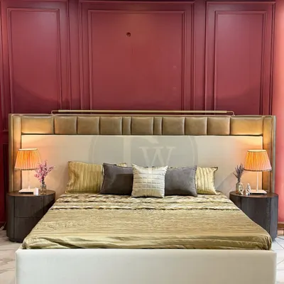 A luxury bed featuring a tall, multi-panelled headboard with integrated lighting. Paired with dark wood side tables and set against a dramatic burgundy wall, this design creates a hotel-like, opulent bedroom experience.