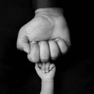 A powerful black and white image of a newborn's tiny fist held against their parent's larger one. The high contrast and simple composition make this a striking and symbolic photo.
