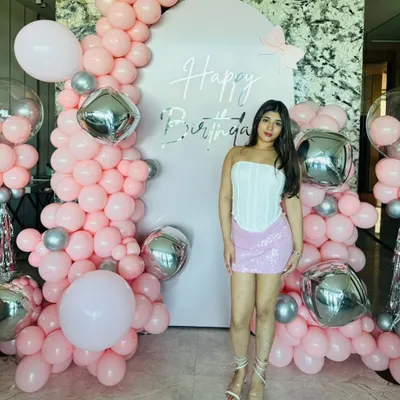 Main character energy for a home birthday party. This setup features a pink backdrop with silver lettering, framed by an organic garland of pink and silver balloons for a fun and glamorous look.