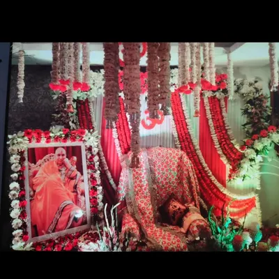 A classic red and white themed stage for a Guruji Satsang. This decoration features a draped backdrop, hanging tuberose garlands, and a floral frame for Guruji's portrait.