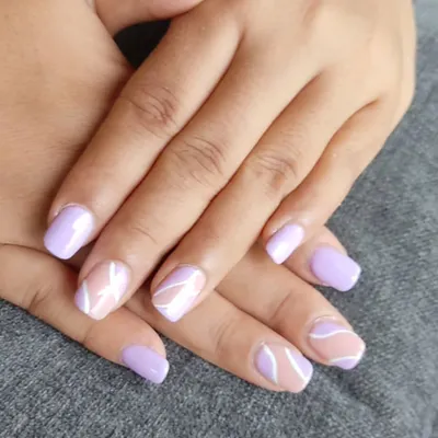 This stylish set features a mix of solid lavender nails and accent nails with abstract white swirls on a nude base. The combination is modern, soft, and artistic.