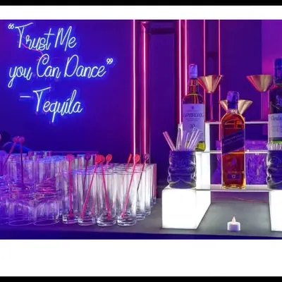 Let the bar do the talking. A neon sign with a fun quote like 'Trust Me you Can Dance - Tequila' instantly sets a playful, high-energy tone for a sangeet or cocktail party.