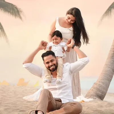 A classic family portrait on the beach, with a beautiful sunset sky. The father holds his son on his shoulders, creating a joyful and timeless image of family love.