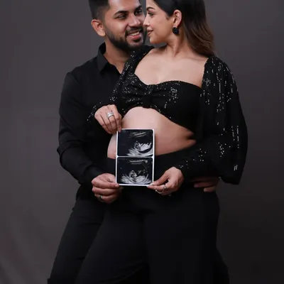 The first look at your little one. This couple proudly holds up their sonogram pictures, a classic and heartwarming way to announce their pregnancy during their modern studio shoot.