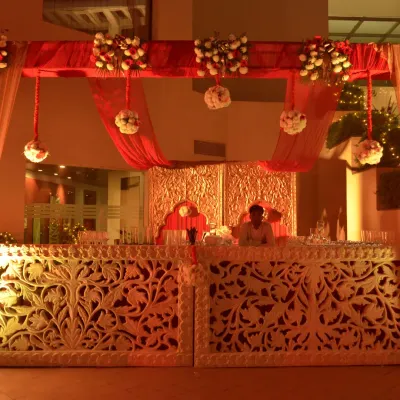 A beautifully crafted bar counter for a traditional wedding. The bar front features intricate white carving, illuminated from within, and is set against a backdrop of ornate golden panels and red drapes.