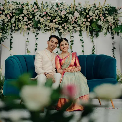A beautiful moment from Sonika and Abhishek's engagement. The couple is seated on a stylish teal sofa against our custom floral wall, a design that combines white and pink blooms with fresh greenery for a soft, romantic feel.