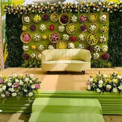 A beautiful Mehendi stage with a backdrop of a green wall decorated with baskets of colorful flowers. This creates a fresh, garden-like feel for photos.