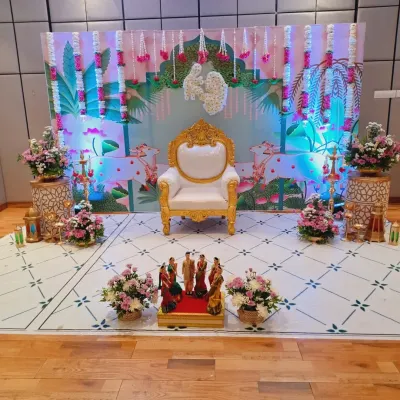A wide view of a Sreemantham setup, showing the main seating area, floral arrangements on pedestals, and decorative props. The printed backdrop with lotus and cow motifs adds a gentle, traditional feel to the modern layout.