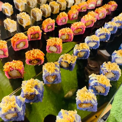 A vibrant platter of assorted sushi rolls, showcasing a beautiful mix of colors, textures, and flavors. From pink and blue rice to crunchy tempura toppings, each piece is a work of art.