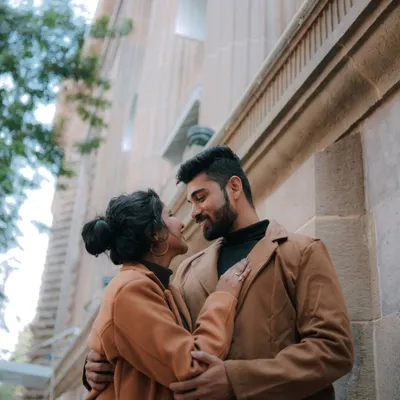 A beautiful, candid shot of a couple embracing in front of the classic architecture of South Mumbai. Their matching coats add a stylish touch to this city pre-wedding photo.