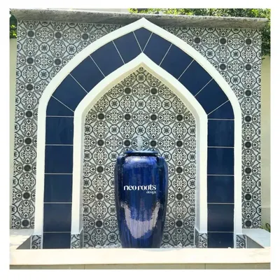 A close-up of a magnificent Moroccan-style water feature. The deep blue ceramic urn and matching arched tilework create a striking visual, while the gentle flow of water adds a calming auditory element to the garden.