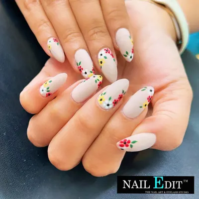 A beautiful and delicate floral design on a matte nude base. The tiny, hand-painted flowers in red, yellow, and white are placed artfully along the sides of the almond-shaped nails for a fresh, garden-inspired look.