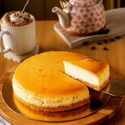 A classic New York cheesecake, beautifully captured for Bisque bakery. The focus is on the creamy texture and golden-brown top, presented simply on a wooden board with a cup of coffee to create a cozy, cafe atmosphere.