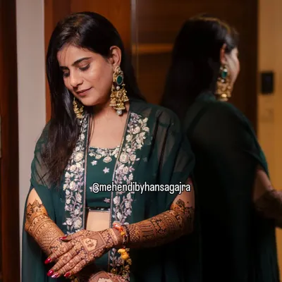 A quiet moment of reflection for the bride, admiring her intricate mehendi. Her elegant green outfit and the warm lighting make this a truly beautiful and emotional shot.