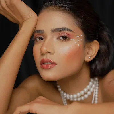 A stunning beauty portrait featuring a model with delicate pearl accents around her eye. The soft lighting and close crop emphasize the flawless makeup and the elegance of the pearl theme.