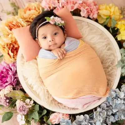 An awake and alert baby girl, wrapped in pastel colors and lying in a bowl surrounded by a beautiful ring of flowers.