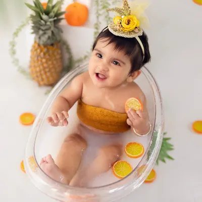 A happy splash! This baby girl is loving her 9-month milestone fruit bath session, surrounded by cheerful oranges and pineapple props.