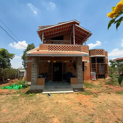 A full view of our completed eco-friendly farmhouse project. The design incorporates a multi-level roof and a welcoming porch with stone pillars, showcasing a blend of traditional and sustainable architecture.