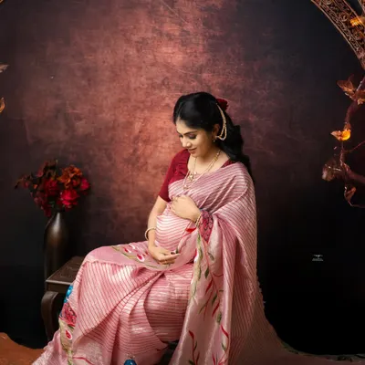 A quiet moment of connection. Seated gracefully in a beautiful pink saree, this mother-to-be gently holds her belly, creating a portrait of pure serenity and love.