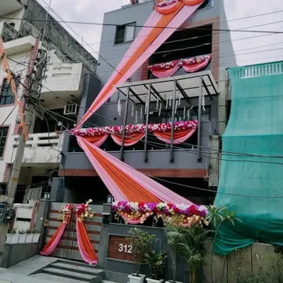 Another example of a full house front decoration for a wedding. I used long, flowing drapes in pink and orange, along with floral garlands on the balconies and gate, to give the home a festive look.