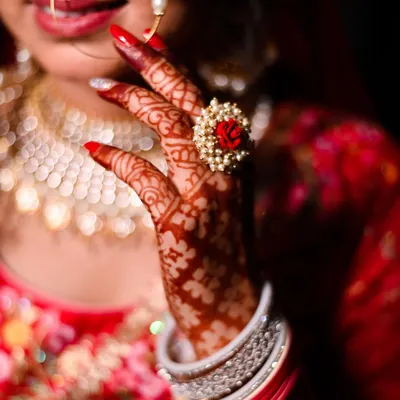 A close-up on the bride's hand, showcasing her beautiful red nails, intricate henna, and a unique floral ring. It’s these small details that complete the bridal look.