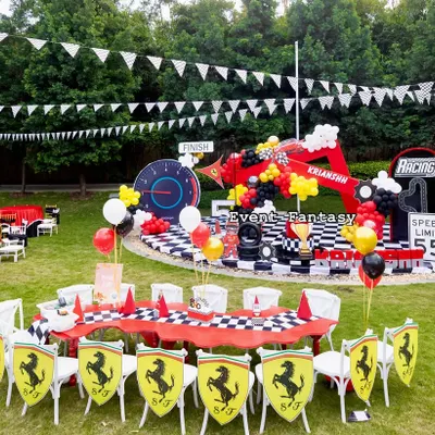A fantastic outdoor Ferrari-themed party for Krianshh. This wide shot shows the main stage, the kids' dining area with custom chairs, and the expansive lawn perfect for racing games.