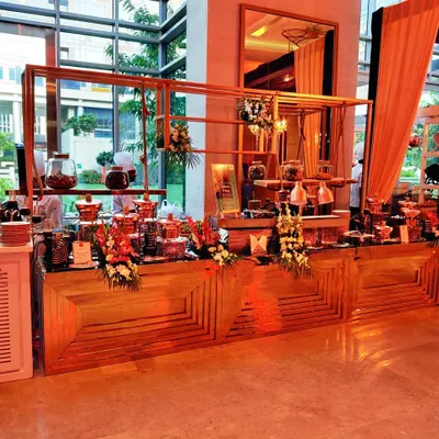 A wide view of our elegant buffet and live station setup for a corporate event. The wooden counters and floral arrangements create a warm and inviting atmosphere for guests.