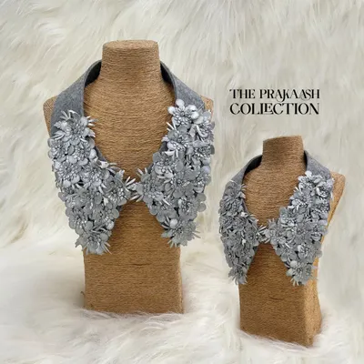This detachable collar is adorned with dozens of silver-grey 3D floral appliques, creating a lush, textured look. It's a sophisticated accessory that adds couture-level detail to any top or dress.