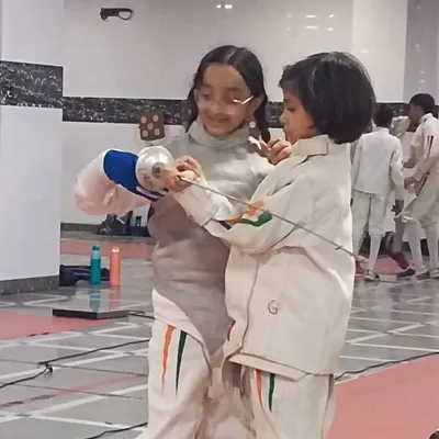 This is what our community is all about. A senior fencer takes the time to guide a younger member, adjusting her grip and sharing valuable experience.