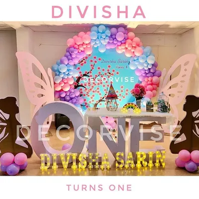 For Divisha's first birthday, we created this beautiful fairy garden stage. The design includes large fairy wing silhouettes, a cherry blossom backdrop, pastel balloon clouds, and illuminated marquee letters spelling out her name.