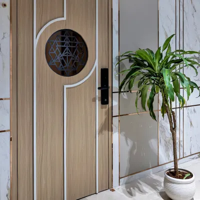 Sometimes, simple is better. This modern entryway is defined by its clean lines, with a statement wooden door featuring a geometric grill, a marble-paneled wall, and a single plant for a touch of life.