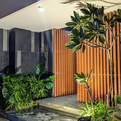 A modern home entrance featuring a striking combination of wood slats, dark tiles, and lush greenery. A small water channel and strategic lighting create a sophisticated and welcoming first impression.