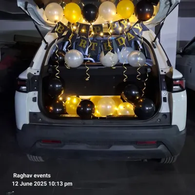 A classic car boot birthday surprise. The decoration includes a 'Happy Birthday' banner, fairy lights, and balloons in black, gold, and silver.