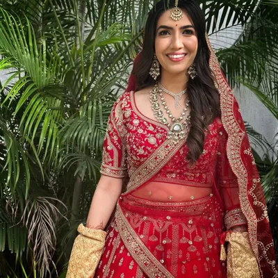 A classic North Indian bridal look. Draped in a magnificent red lehenga, her makeup is radiant and glowing, with defined eyes and a soft lip, letting her joyful smile be the focus.