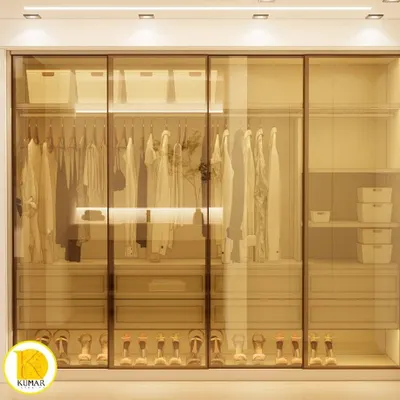 A stunning walk-in closet with tinted glass sliding doors and internal lighting. This custom modular wardrobe provides a clear view of the organized clothes and accessories, adding a touch of luxury to the bedroom.