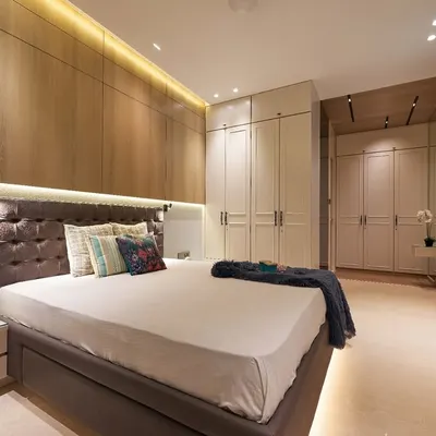 This master bedroom combines warm wood paneling on the feature wall with sleek, off-white wardrobes. We used integrated LED strip lighting above the headboard and below the bed to create a soft, ambient glow and a floating effect.