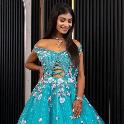 A closer look at our stunning off-the-shoulder blue gown. The intricate lacework on the corset-style bodice and the scattered floral details on the tulle skirt are designed for a true princess moment.