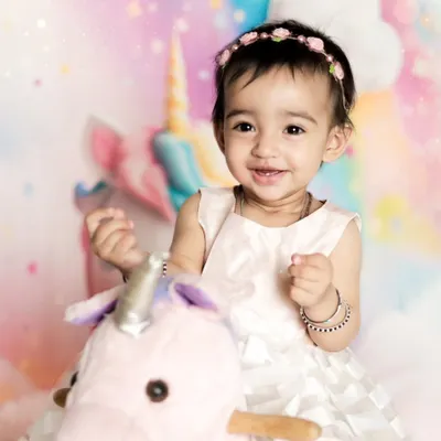 A close-up of this sweet girl's happy smile during her unicorn-themed photoshoot. The pastel rainbow background and her gentle expression make this a truly magical portrait.
