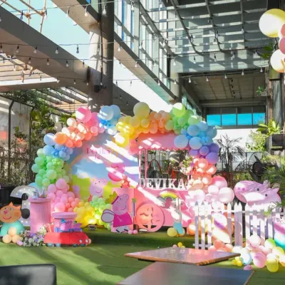 A full view of the vibrant Peppa Pig themed party, showcasing the colorful balloon arch, character props, and a custom dessert cart, all set up in a bright, open venue.
