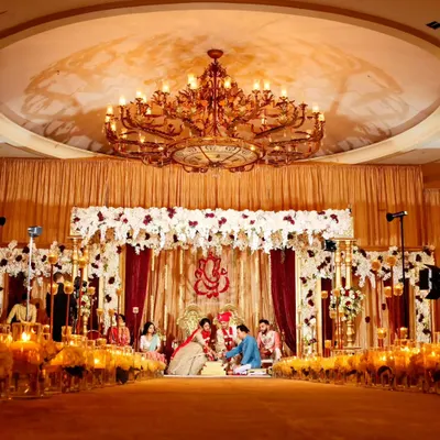 A traditional Hindu wedding ceremony under a grand chandelier in our ballroom. The space is designed to accommodate large gatherings while maintaining a sense of warmth and intimacy, with golden drapery and floral arrangements creating a sacred and celebratory atmosphere.