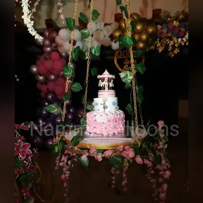 A unique cake display can be a centerpiece of the party. Here, a beautiful birthday cake is presented on a swing decorated with flowers and vines, adding a touch of magic to the celebration.