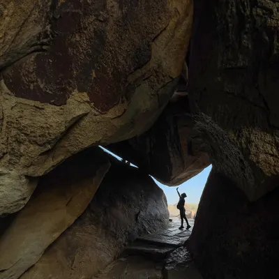 A traveler's silhouette is framed by a natural cave opening, reaching up towards the sky. This photograph captures the sense of adventure and discovery that Hampi's unique landscape inspires.