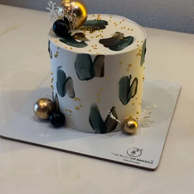 This cake showcases a modern, minimalist aesthetic with abstract buttercream strokes in muted tones. Accented with gold leaf and decorative spheres, it's a sophisticated choice for milestone birthdays, anniversaries, or any contemporary celebration.