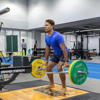 A runner performs a trap bar deadlift, an excellent exercise for building lower body and core strength, which is fundamental for powerful running. Our program incorporates key lifts to build a strong foundation.