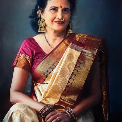 A portrait capturing the quiet dignity of a mother dressed in a traditional silk sari. The soft lighting and painterly background highlight her classic jewelry and serene expression, creating a timeless family treasure.