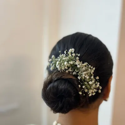 A classic and elegant low bun adorned with delicate baby's breath. This timeless hairstyle is perfect for a sophisticated look for a wedding or reception.