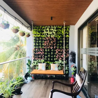 The final result of a balcony transformation. We installed a full-height vertical garden as a stunning backdrop for a wooden swing, complemented by potted plants and hanging baskets to create a lush, private oasis.